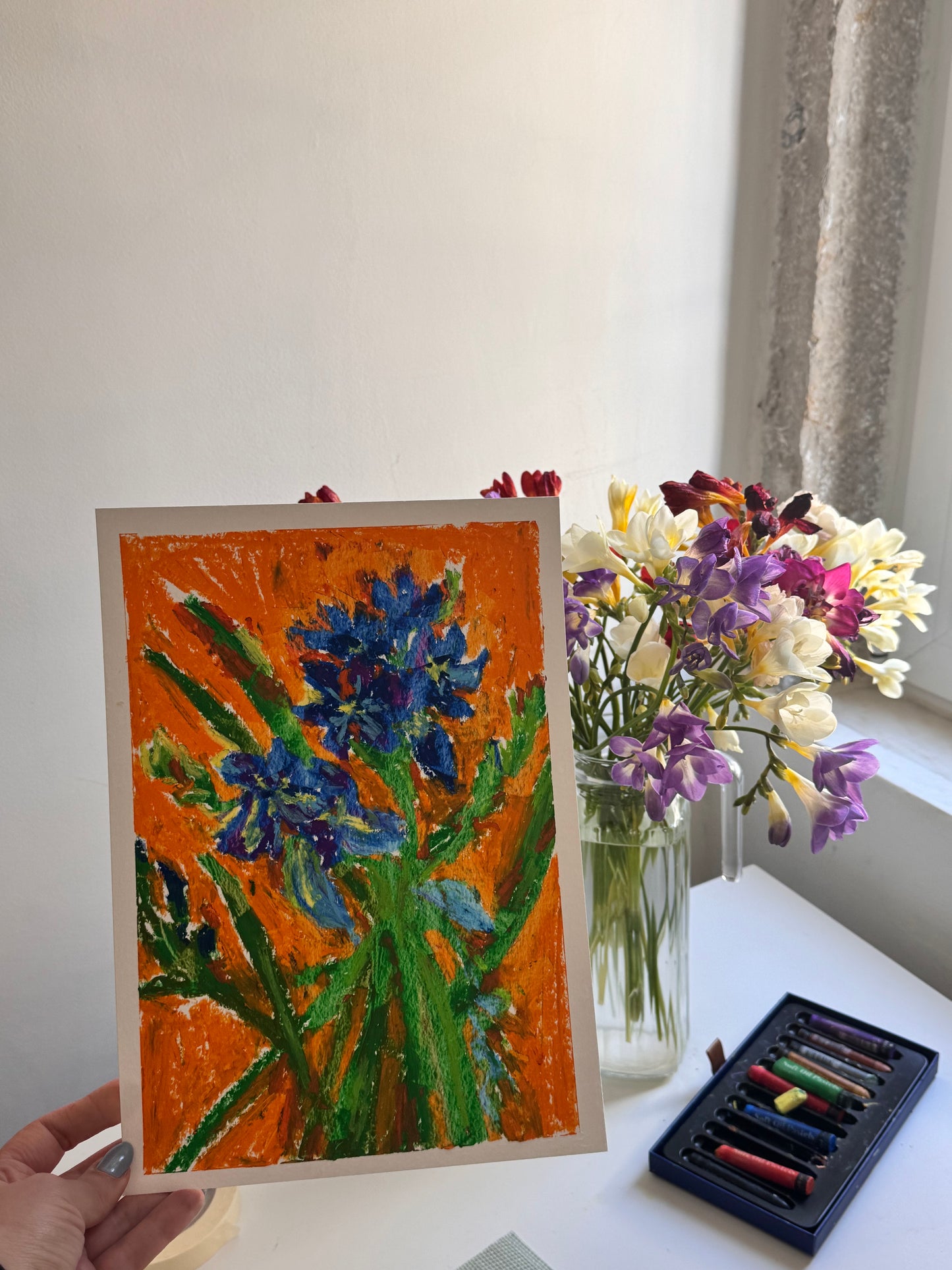 Artistic depiction of flowers on a card next to a vase with real flowers and art supplies.